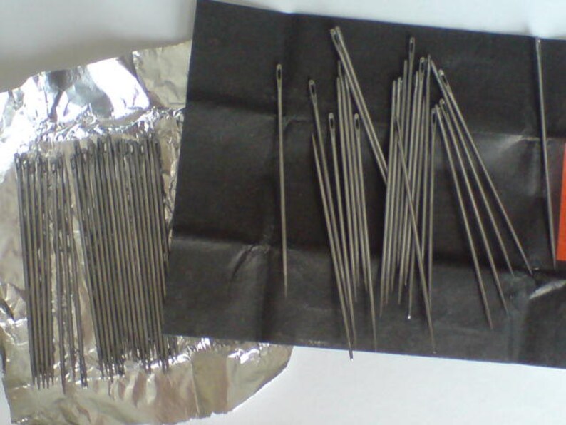 May include: Two packages of silver sewing needles. One package is wrapped in aluminum foil and the other is wrapped in black paper.