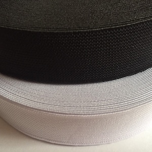 Peut inclure: Deux rouleaux d'élastique, un noir et un blanc. L'élastique est tissé et a une surface texturée.