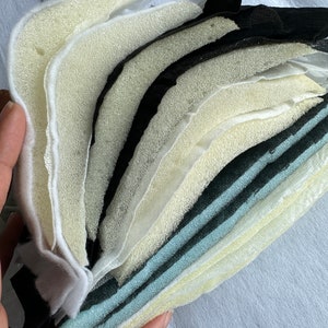 May include: A stack of different colored and textured foam sheets. The sheets are layered on top of each other and are being held by a hand.