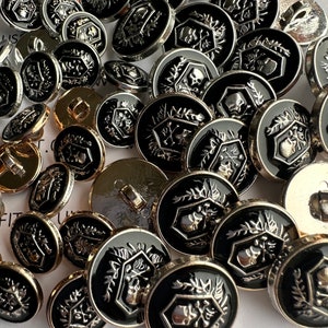 Puede incluir: Primer plano de un grupo de botones de calavera negros y plateados. Los botones son redondos y tienen un diseño de calavera en relieve con huesos cruzados. Los botones están rodeados por un borde plateado.