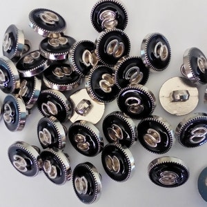 May include: A collection of black and silver buttons with a decorative design. The buttons have a raised, silver-colored design on a black background.