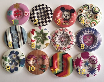 Può includere: Dodici bottoni di legno diversi con vari disegni colorati. I bottoni sono numerati da 1 a 12. Alcuni disegni includono strisce, fiori, Topolino e un motivo a scacchi.