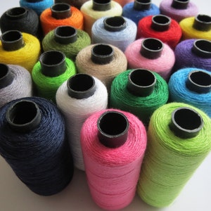 May include: A collection of spools of thread in various colours, including blue, green, pink, yellow, and purple. The spools are arranged in a semi-circle on a white surface.