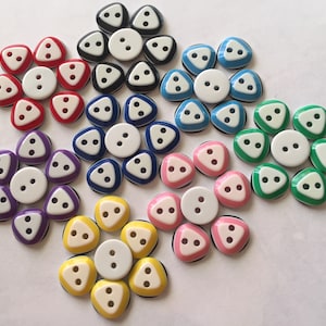 May include: Assortment of colorful triangle-shaped buttons with white centers and black trim. The buttons have three holes each.