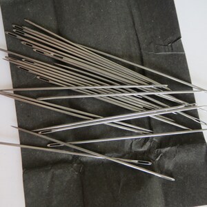 May include: A bundle of silver sewing needles on a black background.
