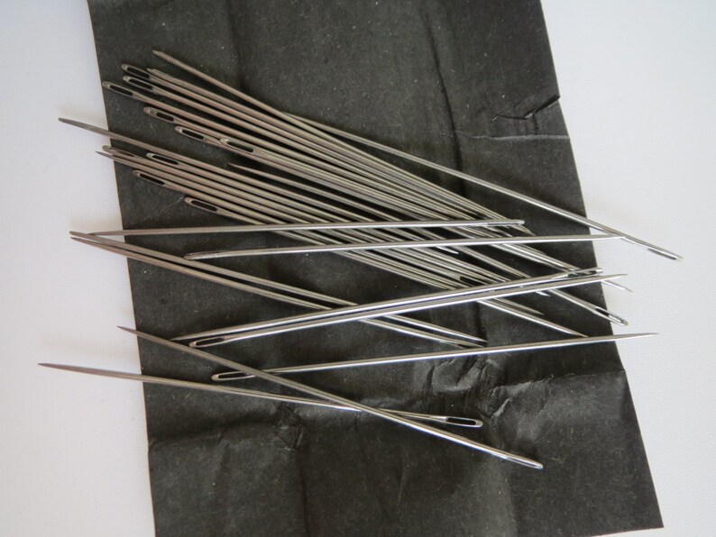 May include: A bundle of silver sewing needles on a black background.