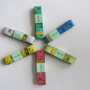May include: Five different colored measuring tapes with green, blue, yellow, red, and white labels. The labels have the text "80 inch/150 cm" and "Black 75cm".