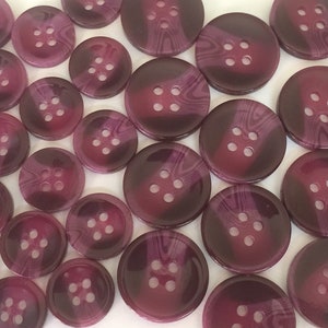 May include: A collection of 20 purple buttons with a swirl pattern. The buttons have four holes each.