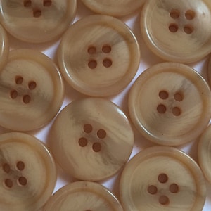 May include: A collection of beige buttons with four holes each. The buttons have a subtle marbled pattern and a smooth, glossy finish.