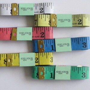 May include: Five different colored measuring tapes with a black and white measuring scale. The tapes are labeled with "60 INCH/150CM" and "GLASS".