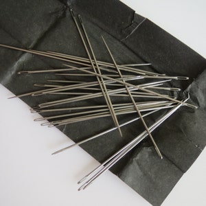 May include: A close-up of a pile of silver sewing needles on a black paper background.