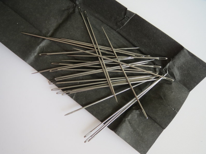 May include: A close-up of a pile of silver sewing needles on a black paper background.