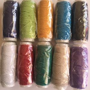 May include: Ten spools of thread in various colors, including purple, green, orange, blue, black, white, red, teal, beige, and lavender. The spools are wrapped in clear plastic.