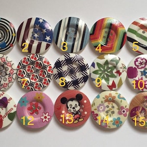 May include: Fifteen round wooden buttons with various colorful patterns and designs. The buttons feature a variety of themes, including geometric patterns, floral designs, cartoon characters, and abstract art.
