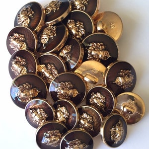 以下が含まれることがあります： 茶色の背景にライオンの頭が浮き彫りになった、金色のボタンが24個あります。ボタンはシャンクバックです。