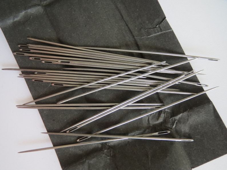 May include: A pile of silver sewing needles on a black surface. The needles are sharp and pointed, and they are arranged in a random pattern.