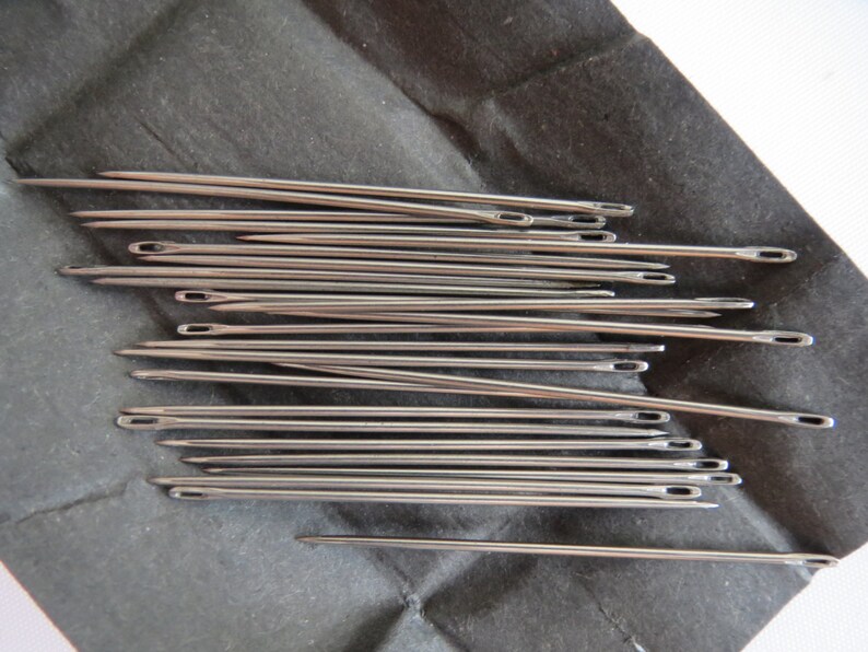 May include: A close-up of a group of silver sewing needles arranged in a pile on a black surface.
