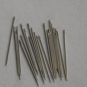 May include: A group of 20 silver needles, arranged in a fan shape on a white surface.