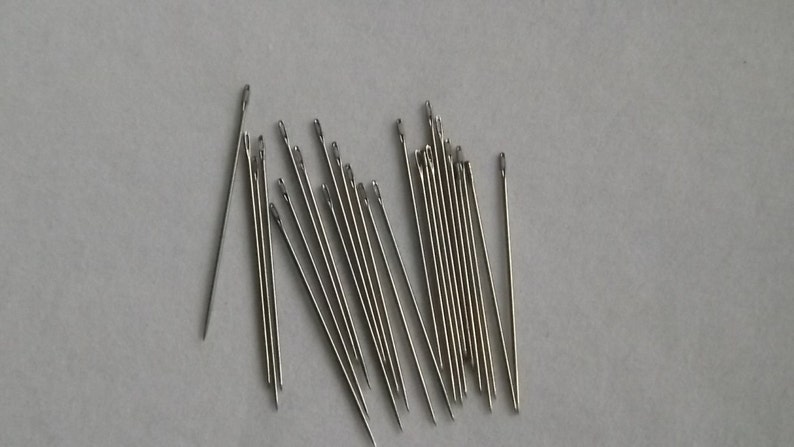 May include: A group of 20 silver needles, arranged in a fan shape on a white surface.