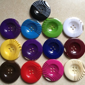 May include: Twelve round buttons with a swirl pattern. The buttons are in various colors, including purple, blue, green, white, yellow, brown, red, pink, and cream.