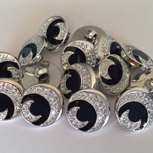 May include: A group of 12 silver and black buttons with a crescent moon design and rhinestones around the edge.
