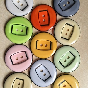 Può includere: Assortimento di 10 bottoni in plastica colorati con due fori ciascuno. I bottoni sono rotondi e hanno un bordo nero. I bottoni sono di vari colori, tra cui bianco, grigio, arancione, verde, giallo, rosa, azzurro e beige.