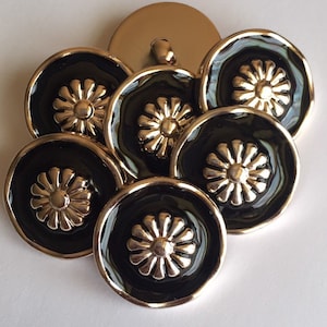 May include: A selection of decorative buttons. The buttons feature a black enamel finish with a gold-coloured floral design in the centre. The buttons are round with a gold-coloured rim and a gold-coloured shank on the back.