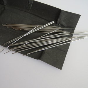 May include: A close-up of a pile of silver sewing needles on a black surface.
