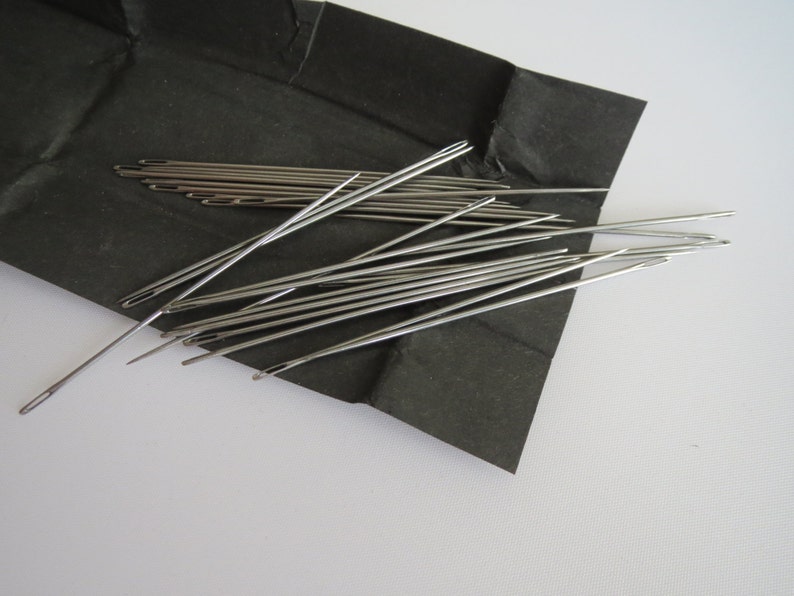 May include: A close-up of a pile of silver sewing needles on a black surface.