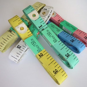May include: A collection of six colorful measuring tapes, each with a different color and marked with inches and centimeters. The tapes are all rolled up and stacked on top of each other.