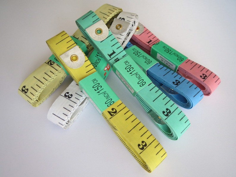 May include: A collection of six colorful measuring tapes, each with a different color and marked with inches and centimeters. The tapes are all rolled up and stacked on top of each other.