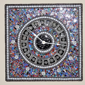 May include: A square mosaic clock with a black face and white hands. The mosaic is made of small, colorful tiles in shades of blue, red, green, and yellow. The clock is surrounded by a black frame with a silver border.