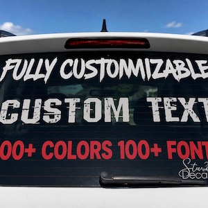 May include: A white and red vinyl decal applied to a car rear window. The text reads FULLY CUSTOMIZABLE in a white brush-stroke font, CUSTOM TEXT in a white distressed block font, and 100+ COLORS 100+ FONTS in red, with a Studio Decals logo.