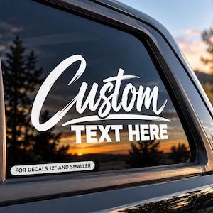 Könnte beinhalten: Ein weißer Vinyl-Aufkleber auf einer Fahrzeugscheibe mit dem Wort Custom in Pinselschrift über den Worten TEXT HERE in fetter serifenloser Schrift. Ein kleines Etikett darunter lautet FOR DECALS 30,48 CM AND SMALLER.