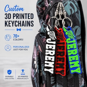 May include: Three custom 3D printed keychains hanging from a backpack, each featuring a wing icon and the name JEREMY in bold capital letters. The keychains are black with white text, red with black text, and blue with bright green text.