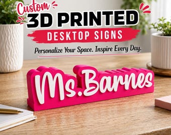 以下が含まれることがあります： 鮮やかなピンク色のベースに白い筆記体でMs. Barnesと書かれた、カスタム3Dプリントのデスクトップサイン。木製の表面に置かれており、上部にはCustom 3D PRINTED DESKTOP SIGNS Personalize Your Space. Inspire Every Day.というテキストが表示されています。