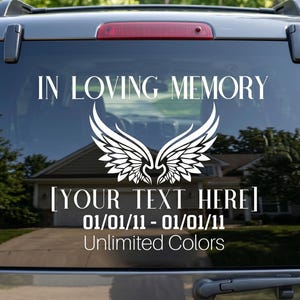 May include: A white vinyl decal applied to a car rear window featuring the text IN LOVING MEMORY, a pair of stylized angel wings, the placeholder text YOUR TEXT HERE, and the date 01/01/11 - 01/01/11 with the additional text Unlimited Colors.