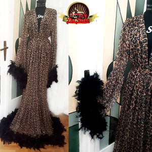 May include: A long, brown and black leopard print robe with black feather trim around the sleeves and hem. The robe has a tie belt and a deep V-neck.