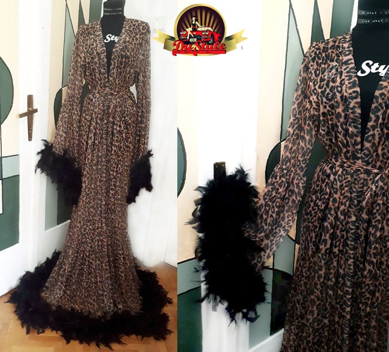 May include: A long, brown and black leopard print robe with black feather trim around the sleeves and hem. The robe has a tie belt and a deep V-neck.