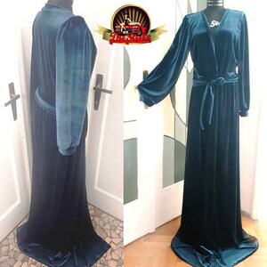 May include: A long teal blue velvet robe with a V-neckline, long sleeves, and a tie belt. The robe has a flowing silhouette and a slight sheen.