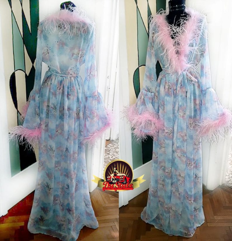 Puede incluir: Una bata larga de color azul claro con estampado floral y ribete de plumas rosas. La bata tiene mangas largas y un lazo en la cintura.