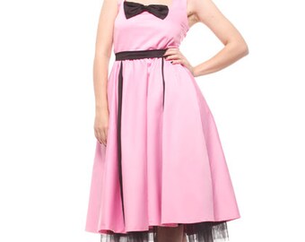Peut inclure: Une femme portant une robe rose avec un nœud noir et une bordure noire. La robe a une jupe ample et une jupon en tulle. Elle porte des talons nus avec des strass.