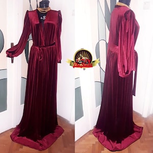 May include: A long, burgundy velvet robe with a V-neckline, long sleeves, and a tie belt. The robe has a flowing, elegant silhouette.