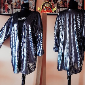 May include: A silver sequined kimono with a long, open front and three-quarter sleeves. The kimono has a subtle striped pattern and is made of a soft, flowing fabric.