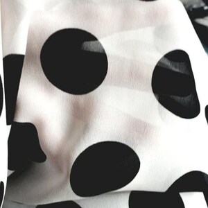 May include: White fabric with black polka dots. The fabric is folded and the polka dots are visible.
