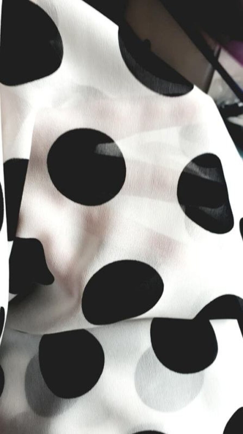 May include: White fabric with black polka dots. The fabric is folded and the polka dots are visible.