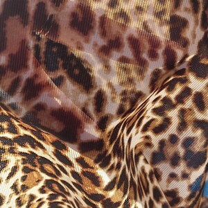 Pu&ograve; includere: Primo piano di un tessuto a stampa leopardata marrone e beige con una trama a rete. Il tessuto &egrave; stropicciato e piegato, creando un aspetto testurizzato.