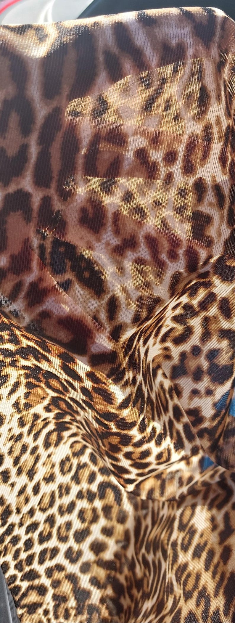 Pu&ograve; includere: Primo piano di un tessuto a stampa leopardata marrone e beige con una trama a rete. Il tessuto &egrave; stropicciato e piegato, creando un aspetto testurizzato.