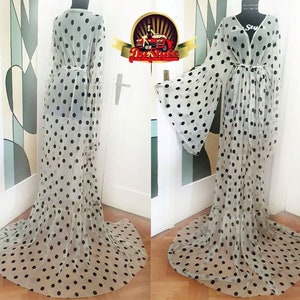 Puede incluir: Un vestido maxi blanco transparente con lunares negros y mangas largas acampanadas. El vestido tiene un escote en V y un lazo en la cintura.