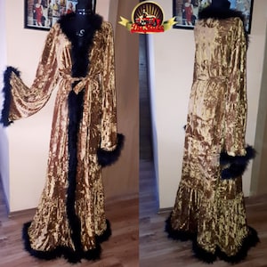 Puede incluir: Una larga bata de terciopelo dorado con ribete de plumas negras alrededor del cuello, las mangas y el dobladillo. La bata tiene un cinturón de lazo y un dobladillo con volantes.